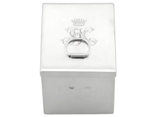 fig 3. A rectangular Victorian sterling silver tea caddy featuring an engraved crest, top folding handle, and visible side hallmarks.