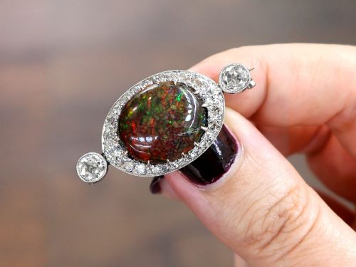 fig 3. An Edwardian platinum brooch featuring an oval cabochon boulder opal surrounded by a halo of diamonds and two outer accent diamonds.