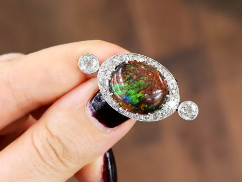 fig 4. An Edwardian platinum brooch featuring an oval cabochon boulder opal surrounded by a halo of diamonds and two outer accent diamonds.