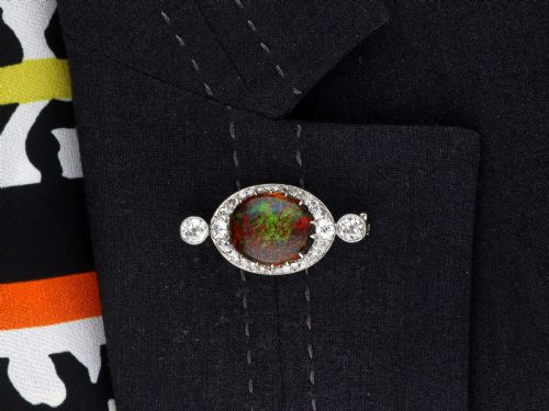 fig 9. An Edwardian platinum brooch featuring an oval cabochon boulder opal surrounded by a halo of diamonds and two outer accent diamonds.