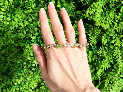 fig 1. An antique Art Nouveau 9ct yellow gold bracelet featuring round-cut green peridots held in collet settings between openwork scroll links.