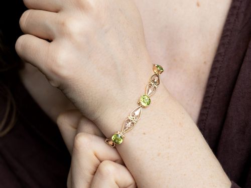 fig 3. An antique Art Nouveau 9ct yellow gold bracelet featuring round-cut green peridots held in collet settings between openwork scroll links.