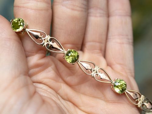 fig 4. An antique Art Nouveau 9ct yellow gold bracelet featuring round-cut green peridots held in collet settings between openwork scroll links.