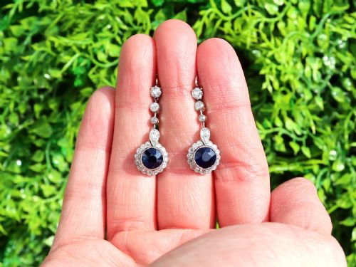 fig 1. A pair of antique Art Deco platinum drop earrings featuring round dark blue sapphires encircled by diamond halos suspended from articulated diamond links.