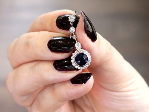 fig 2. A pair of antique Art Deco platinum drop earrings featuring round dark blue sapphires encircled by diamond halos suspended from articulated diamond links.