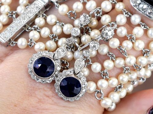fig 4. A pair of antique Art Deco platinum drop earrings featuring round dark blue sapphires encircled by diamond halos suspended from articulated diamond links.