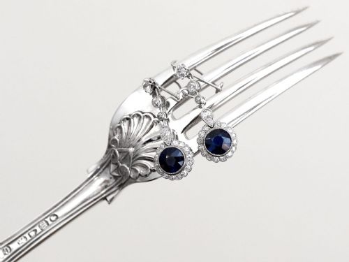 fig 5. A pair of antique Art Deco platinum drop earrings featuring round dark blue sapphires encircled by diamond halos suspended from articulated diamond links.