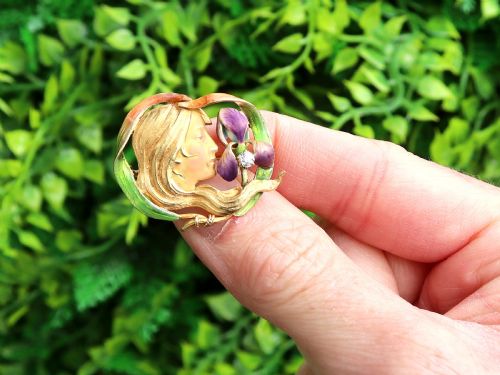 fig 1. An Art Nouveau 18ct yellow gold brooch detailing a maiden profile framed by green enamel foliage and a purple enamelled iris set with a single diamond.