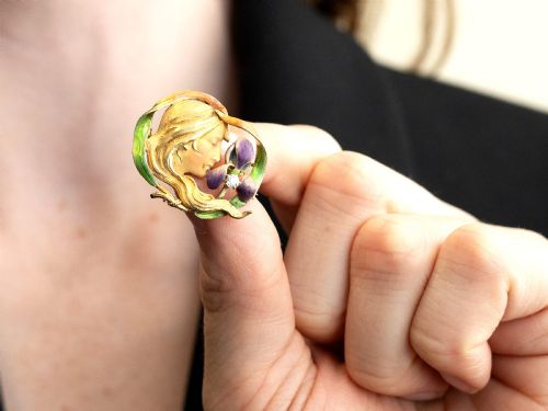 fig 2. An Art Nouveau 18ct yellow gold brooch detailing a maiden profile framed by green enamel foliage and a purple enamelled iris set with a single diamond.