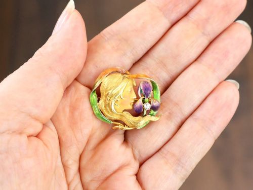fig 3. An Art Nouveau 18ct yellow gold brooch detailing a maiden profile framed by green enamel foliage and a purple enamelled iris set with a single diamond.