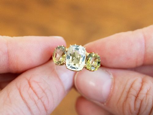 fig 2. A late Victorian 18ct yellow gold trilogy ring featuring a central cushion-cut yellow sapphire flanked by two greenish-yellow chrysoberyl gemstones in claw settings.