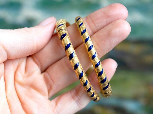 fig 4. A Victorian hinged yellow gold bangle featuring detailed hand engraving, deep blue enamel panels, set diamonds, and graduated natural pearls.
