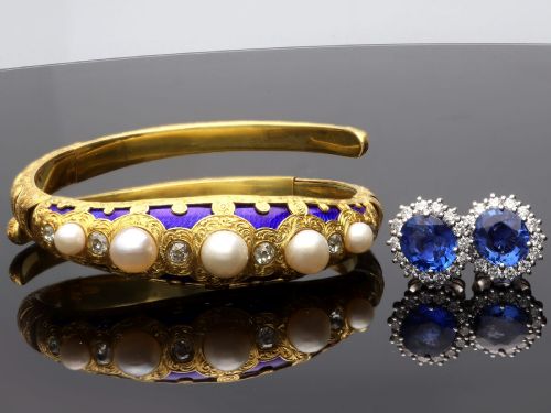 fig 5. A Victorian hinged yellow gold bangle featuring detailed hand engraving, deep blue enamel panels, set diamonds, and graduated natural pearls.