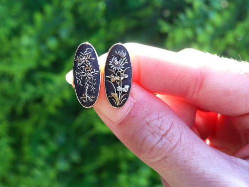 fig 1. A pair of late nineteenth-century double-ended oval cufflinks crafted in 18ct yellow gold, featuring dark patinated shakudo panels with gold and silver botanical relief inlays.