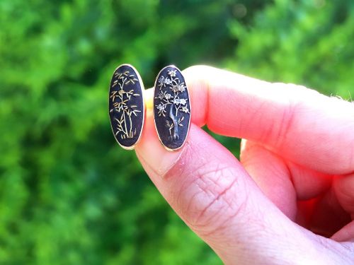 fig 2. A pair of late nineteenth-century double-ended oval cufflinks crafted in 18ct yellow gold, featuring dark patinated shakudo panels with gold and silver botanical relief inlays.
