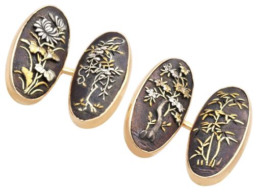 fig 3. A pair of late nineteenth-century double-ended oval cufflinks crafted in 18ct yellow gold, featuring dark patinated shakudo panels with gold and silver botanical relief inlays.
