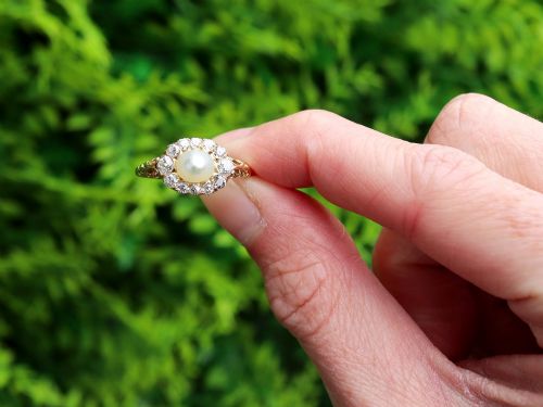 fig 1. An 18ct yellow gold cluster ring featuring a central oval natural pearl surrounded by a halo of old-cut diamonds with scroll-carved shoulders.