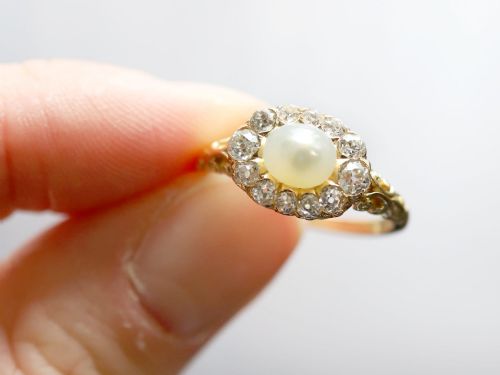 fig 3. An 18ct yellow gold cluster ring featuring a central oval natural pearl surrounded by a halo of old-cut diamonds with scroll-carved shoulders.