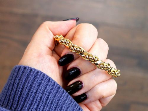 fig 2. An antique Edwardian 15ct gold hinged bangle featuring a twisted ribbon design intertwined around a row of polished gold beads, fitted with a safety chain.
