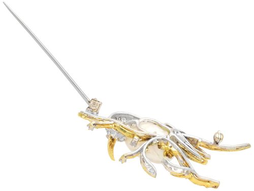 fig 8. An antique 14ct gold bird brooch featuring a blister pearl body, pave diamond head with an emerald eye, perched on a textured gold branch.