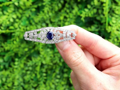 fig 1. An Art Deco 9ct white gold brooch featuring a central oval blue sapphire framed by geometric openwork set with round diamonds.
