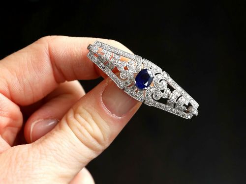 fig 2. An Art Deco 9ct white gold brooch featuring a central oval blue sapphire framed by geometric openwork set with round diamonds.