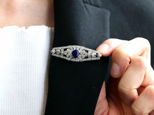 fig 3. An Art Deco 9ct white gold brooch featuring a central oval blue sapphire framed by geometric openwork set with round diamonds.