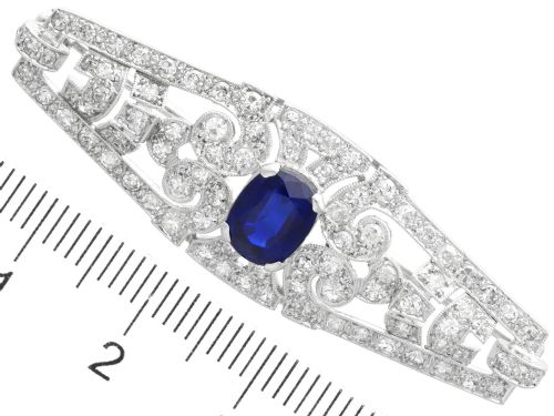 fig 8. An Art Deco 9ct white gold brooch featuring a central oval blue sapphire framed by geometric openwork set with round diamonds.