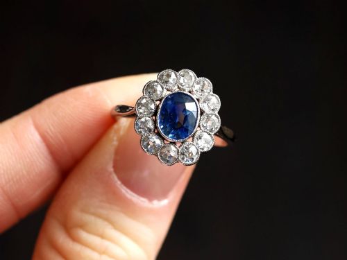 fig 2. An antique platinum cluster ring featuring a central oval blue sapphire framed by twelve round cut diamonds with millegrain detail.