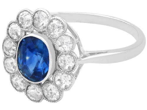 fig 5. An antique platinum cluster ring featuring a central oval blue sapphire framed by twelve round cut diamonds with millegrain detail.