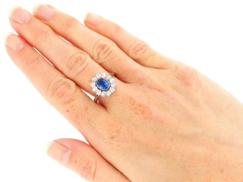 fig 9. An antique platinum cluster ring featuring a central oval blue sapphire framed by twelve round cut diamonds with millegrain detail.
