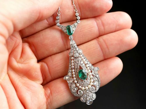 fig 2. An openwork platinum pendant featuring an elongated drop shape set with diamonds, a line of seed pearls, and two vibrant green Colombian emeralds.