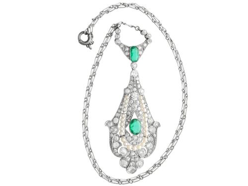 fig 7. An openwork platinum pendant featuring an elongated drop shape set with diamonds, a line of seed pearls, and two vibrant green Colombian emeralds.