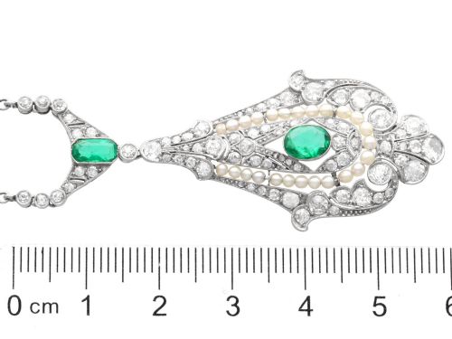 fig 10. An openwork platinum pendant featuring an elongated drop shape set with diamonds, a line of seed pearls, and two vibrant green Colombian emeralds.