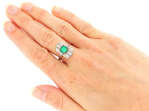 fig 6. An Art Deco 14ct white gold ring featuring a central round green emerald framed by geometric shoulders set with small brilliant diamonds.
