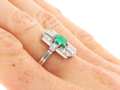 fig 7. An Art Deco 14ct white gold ring featuring a central round green emerald framed by geometric shoulders set with small brilliant diamonds.