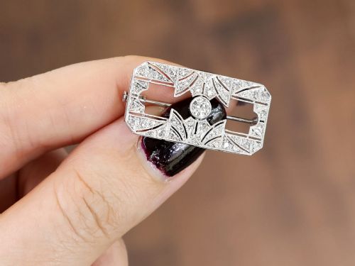 fig 2. A rectangular Art Deco 18ct white gold brooch featuring openwork geometric filigree, millegrain edging, and a central round-cut diamond.