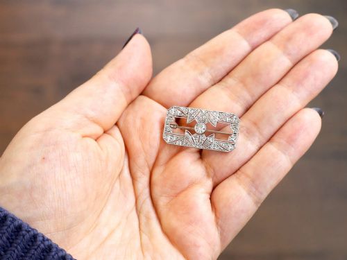 fig 4. A rectangular Art Deco 18ct white gold brooch featuring openwork geometric filigree, millegrain edging, and a central round-cut diamond.