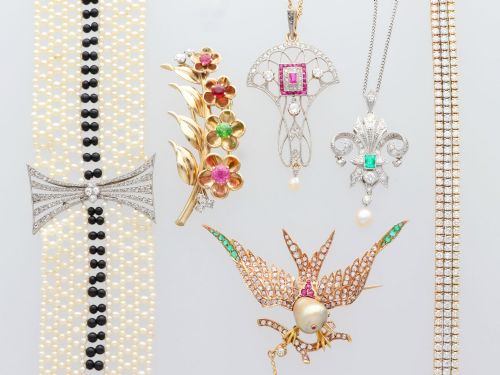 fig 5. An Art Deco platinum pendant shaped as a stylised fleur-de-lis, embellished with pave-set diamonds, a central rectangular emerald, and a hanging pearl drop.