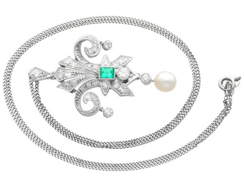 fig 6. An Art Deco platinum pendant shaped as a stylised fleur-de-lis, embellished with pave-set diamonds, a central rectangular emerald, and a hanging pearl drop.