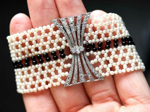 fig 2. An Art Deco multi-strand pearl and black onyx cuff bracelet featuring a central geometric bow-shaped platinum mount set with diamonds.