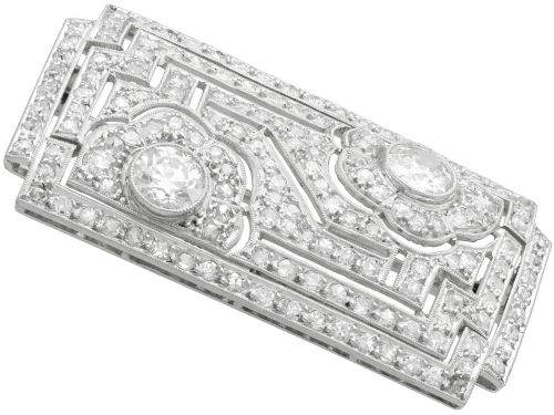 fig 5. A rectangular Art Deco platinum brooch featuring geometric openwork encrusted with round diamonds and two central bezel-set accent diamonds.