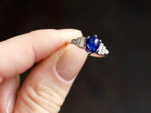 fig 3. An Art Deco platinum dress ring set with a central oval cabochon blue sapphire flanked by stepped geometric shoulders of baguette cut diamonds.