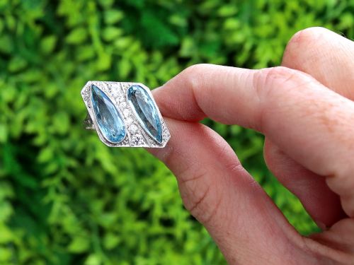 fig 1. An Art Deco platinum cocktail ring featuring two pear-cut light blue aquamarines set diagonally beside a central row of round diamonds with millegrain borders.