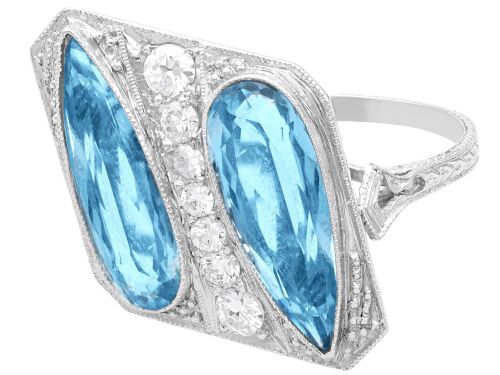 fig 5. An Art Deco platinum cocktail ring featuring two pear-cut light blue aquamarines set diagonally beside a central row of round diamonds with millegrain borders.