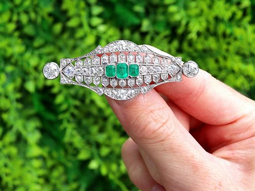 fig 1. An Art Deco platinum brooch featuring three central step-cut green emeralds surrounded by a geometric lattice of diamonds with millegrain borders.