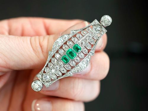 fig 2. An Art Deco platinum brooch featuring three central step-cut green emeralds surrounded by a geometric lattice of diamonds with millegrain borders.