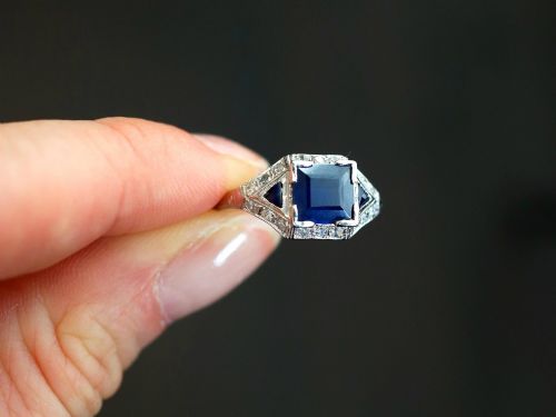 fig 2. An Art Deco platinum ring featuring a central rectangular step-cut blue sapphire flanked by triangular sapphires and diamond-set shoulder details.