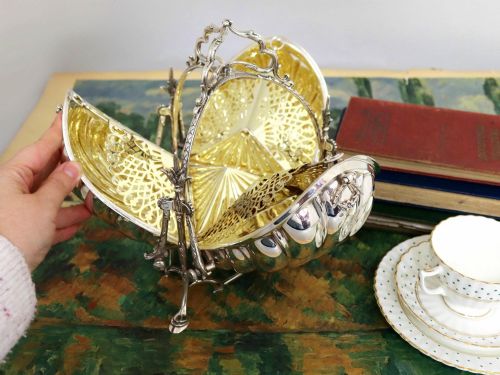 fig 3. An antique Victorian sterling silver folding biscuit box featuring shell-form compartments, an ornate looped handle, and an engraved 1897 monogram.