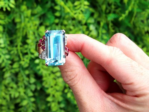 fig 1. A 1940s Retro rose gold cocktail ring set with a large emerald-cut aquamarine flanked by ruby clusters and diamond accents.